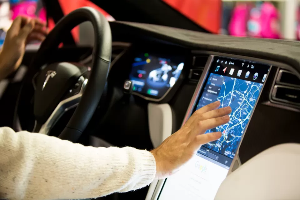 The interior of a Tesla, with a large video screen. The person behind the wheel is touching the screen.
